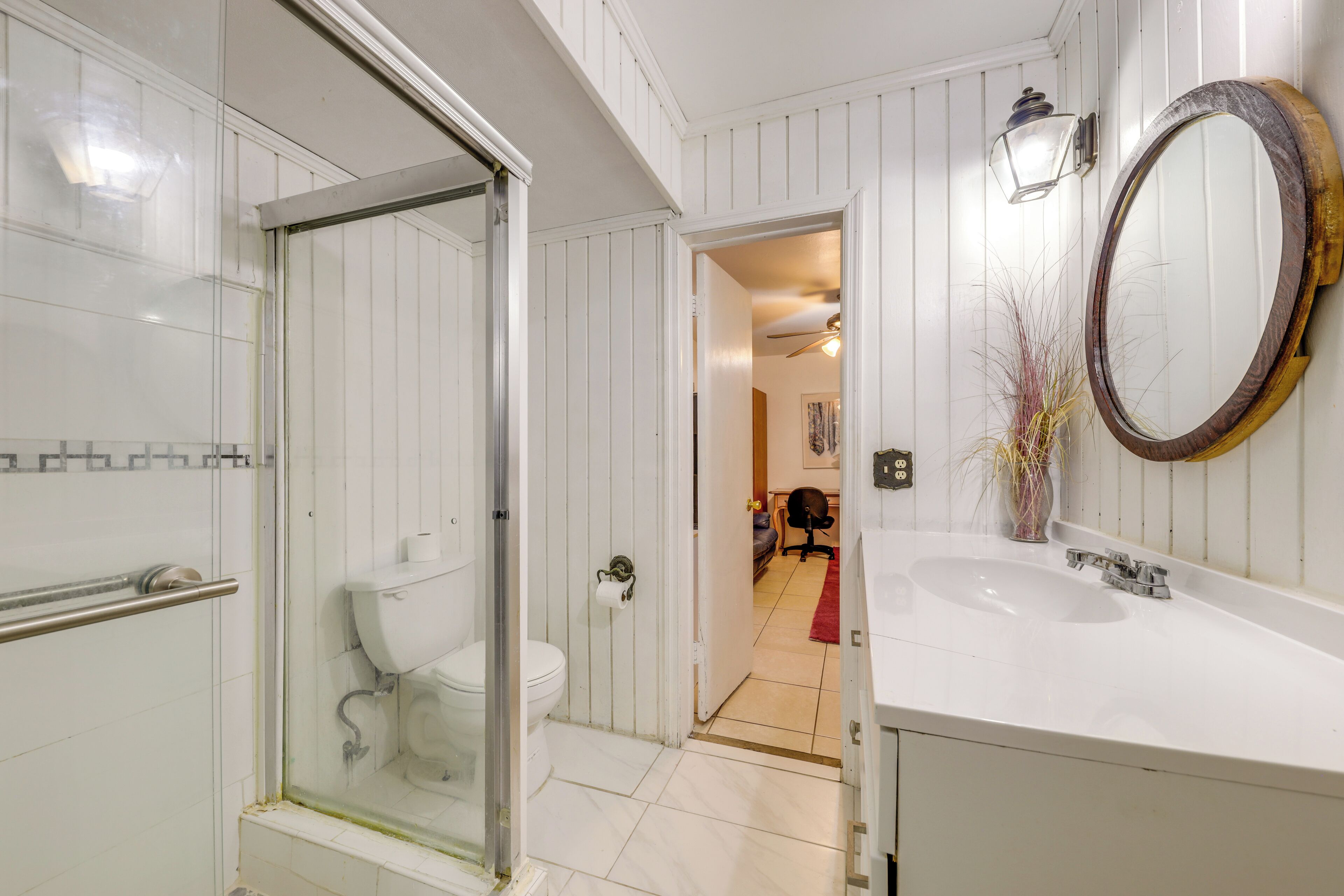 A bathroom with a glass-enclosed shower, a white sink, and a wooden-framed mirror.