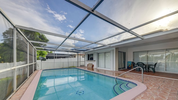 Une piscine intérieure couverte avec un toit en verre, un espace patio avec une table et des chaises, et une vue sur le ciel.