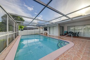 Ein überdachter Pool mit Glasdach, eine Terrassenfläche mit Tisch und Stühlen und Blick zum Himmel.