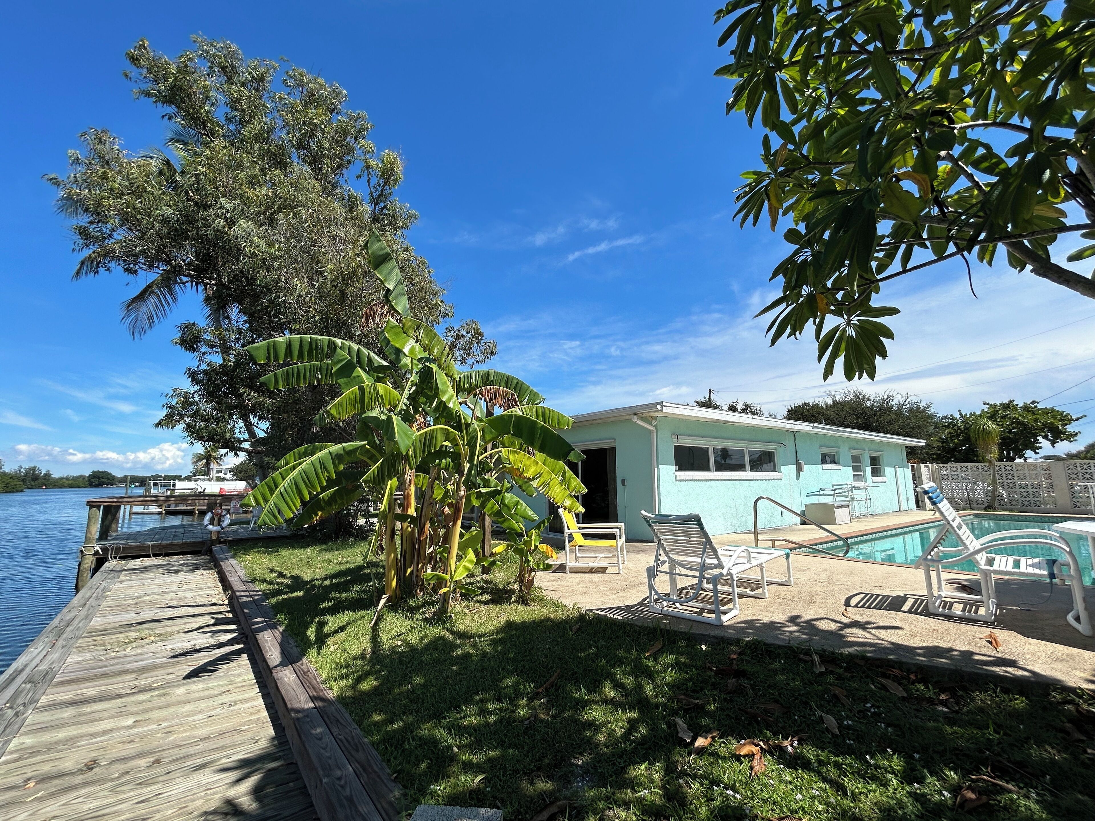 A waterfront property with a dock, a pool, and a small building with a door open.
