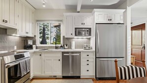 A modern kitchen with white cabinets, stainless steel appliances, and a window with a view of trees.