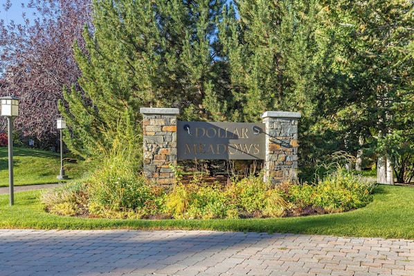 A sign for Dollar Meadows with stone pillars and a landscaped garden.
