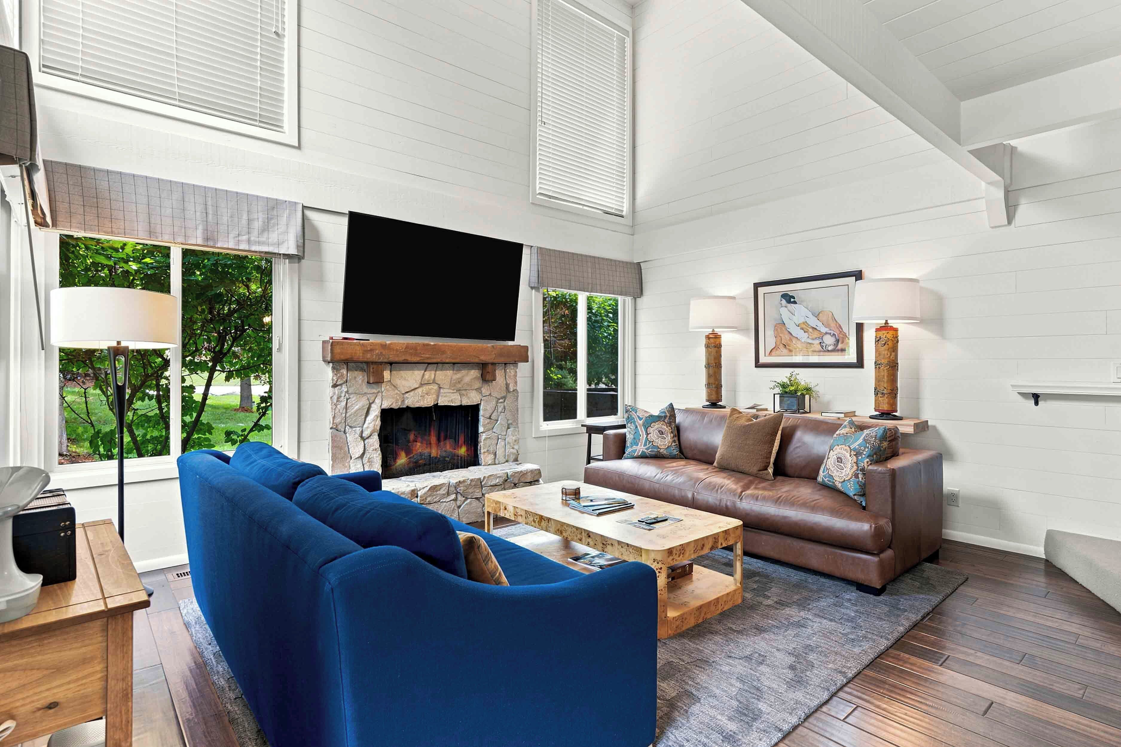 A living room with a stone fireplace, a blue sofa, a brown leather couch, and a flat-screen TV mounted above the fireplace.