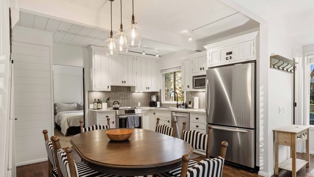 A modern kitchen with white cabinetry, stainless steel appliances, and a wooden dining table with striped chairs.