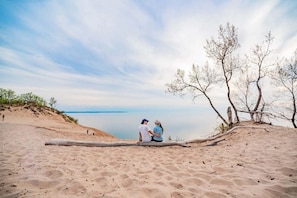 Une plage de sable où deux personnes sont assises sur une bûche, dominant une étendue d’eau calme.