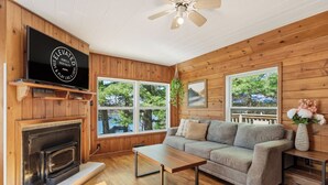 A wooden interior with a fireplace, sofa, TV, and large windows.