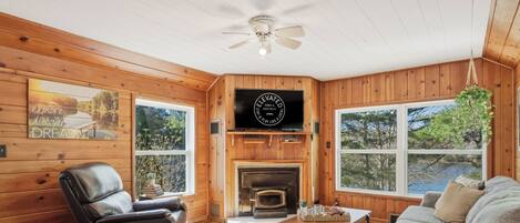 A wooden interior with a fireplace, leather recliner, and large windows.