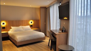 A modern hotel room with a wooden bed, a desk, and a television. - Node Hotel (Manizales)