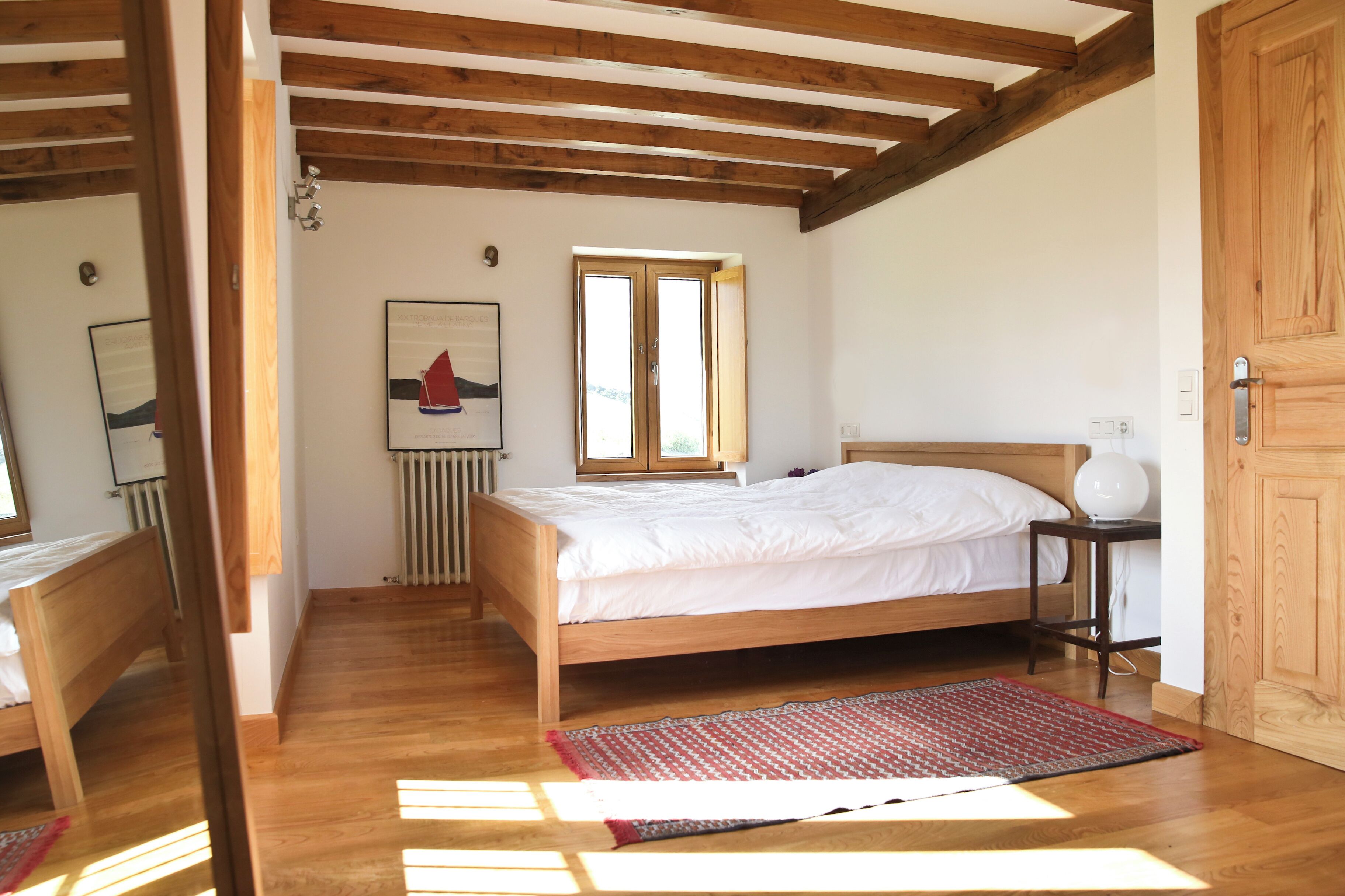 A bedroom with a wooden bed, a red rug, a window, and a radiator.