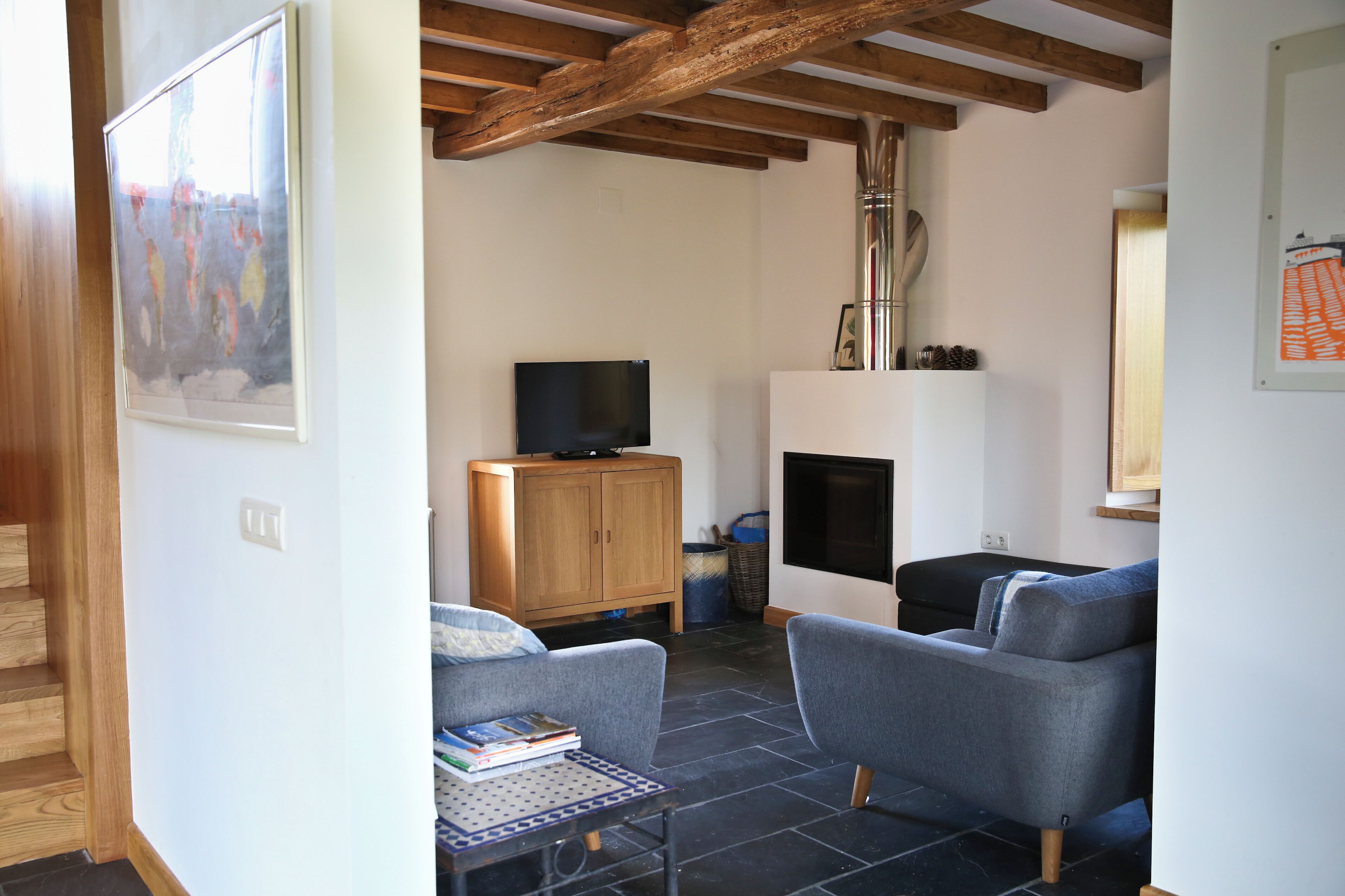 Ein Wohnzimmer mit Kamin, einem Fernseher auf einer Holzkommode und zwei grauen Sesseln.