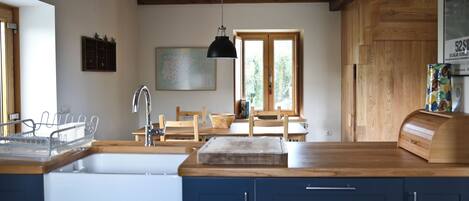 A kitchen with wooden beams, a sink, cabinets, a dining table with chairs, and a hanging light fixture.