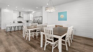 A modern kitchen with white cabinetry, a central island, and a dining area with a wooden table and white chairs. - Ellis Sands with LSV, Arcade, and Billiards (Miramar Beach)