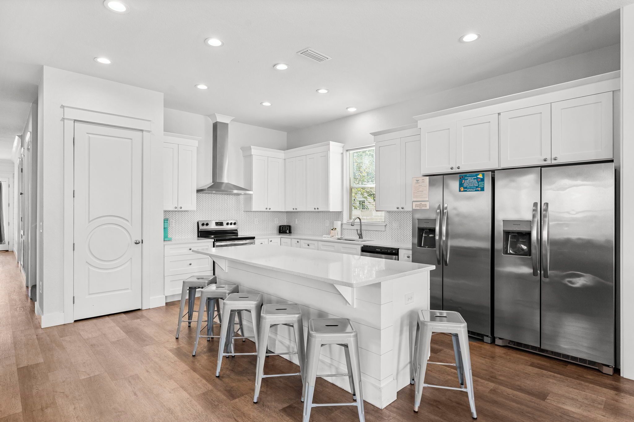 A modern kitchen with white cabinetry, stainless steel appliances, and a central island with bar stools.