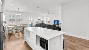 A spacious kitchen with a central island, wooden flooring, and a dining area with white furniture. - Ellis Tide with LSV, Arcade, and Billiards (Miramar Beach)