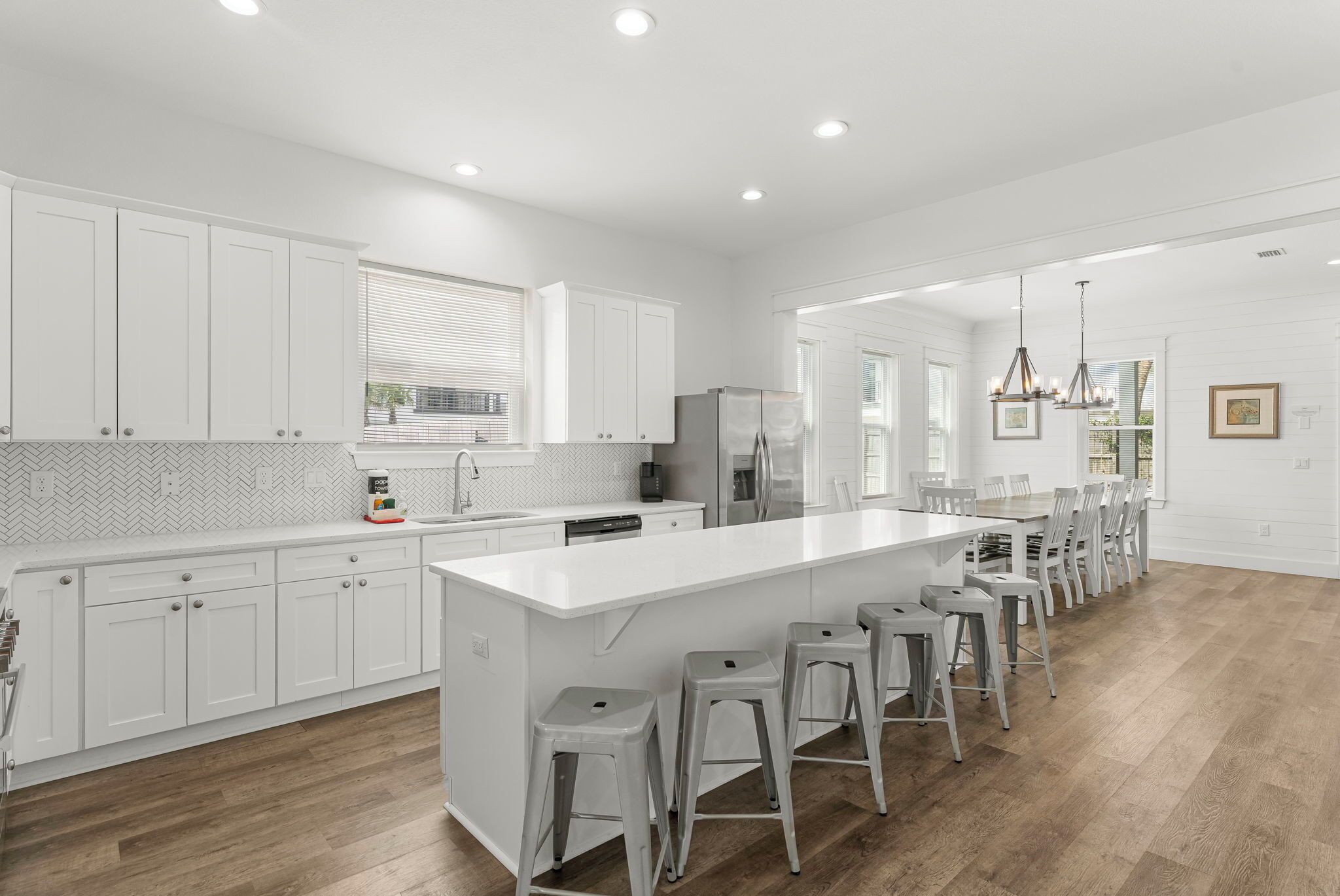 A modern kitchen with white cabinetry, a large island with stools, and a dining area with chairs.
