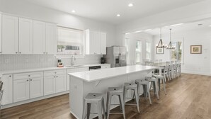 Une cuisine moderne avec des meubles blancs, un grand îlot central doté de tabourets et un coin repas avec des chaises.