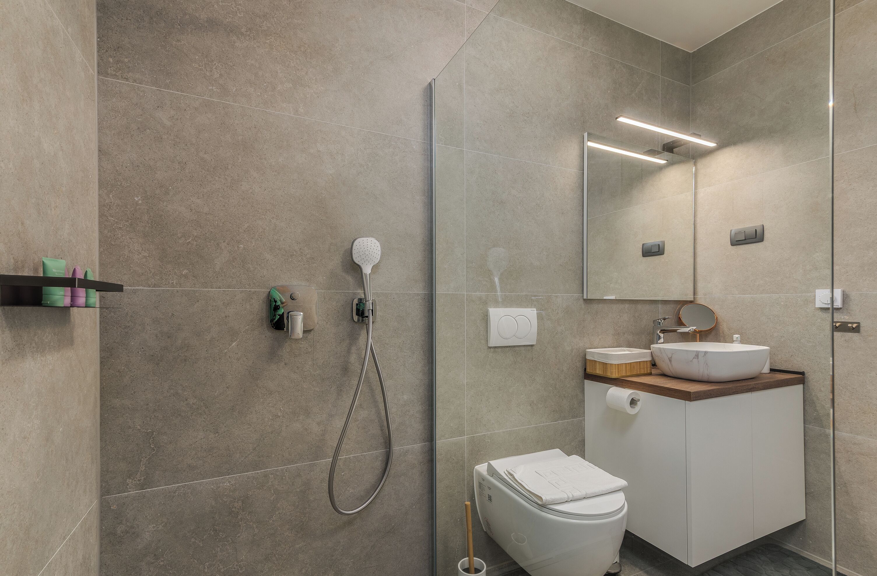 Une salle de bain moderne avec une douche à parois de verre, un lavabo blanc doté d’un plan de toilette en bois et des toilettes.
