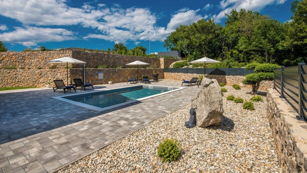 A swimming pool with lounge chairs and umbrellas, surrounded by a stone wall and greenery. - Villa Taralis with heated pool (Kvarner - Kornić) (Kornić)