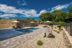 A swimming pool with lounge chairs and umbrellas, surrounded by a stone wall and greenery. - Villa Taralis with heated pool (Kvarner - Kornić) (Kornić)