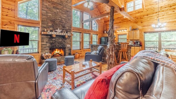 Interior acogedor de una cabaña de madera con chimenea, asientos de cuero y un televisor.
