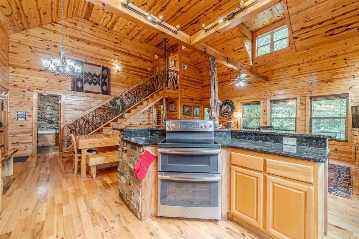 Interior de una cabaña de madera con cocina, comedor y una escalera que sube a un altillo.