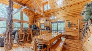 Interior de una cabaña de madera con comedor, cocina y ventanas amplias.