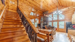 Un interior de madera con una escalera, un comedor y ventanas amplias.