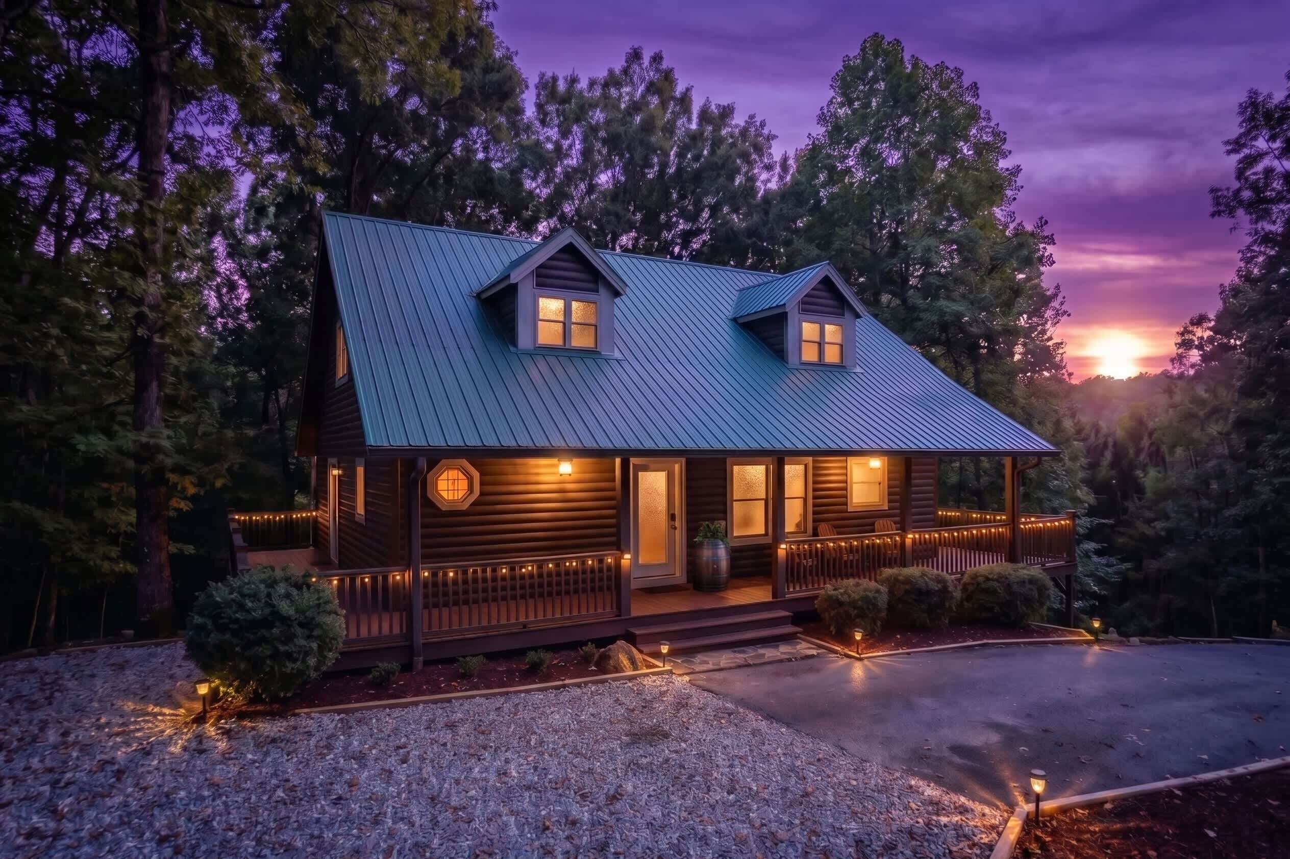 A two-story log cabin with a metal roof, a porch with string lights, and a gravel driveway.