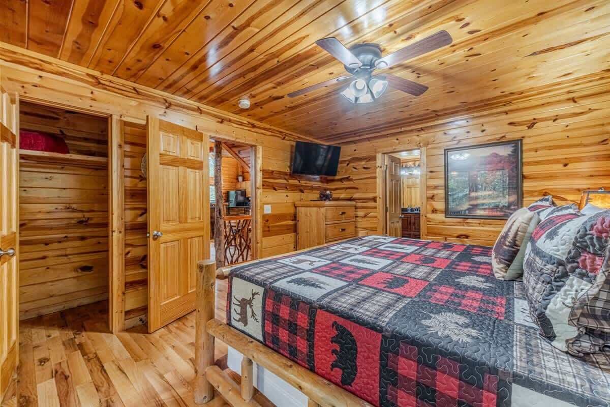 Een blokhutkamer met een bed, houten wanden, een plafondventilator, een televisie en een ingelijst schilderij.