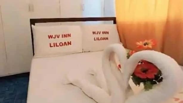 A hotel room with a bed, pillows with text, a painting, and a bouquet of flowers. - WJV INN LILOAN (Liloan)