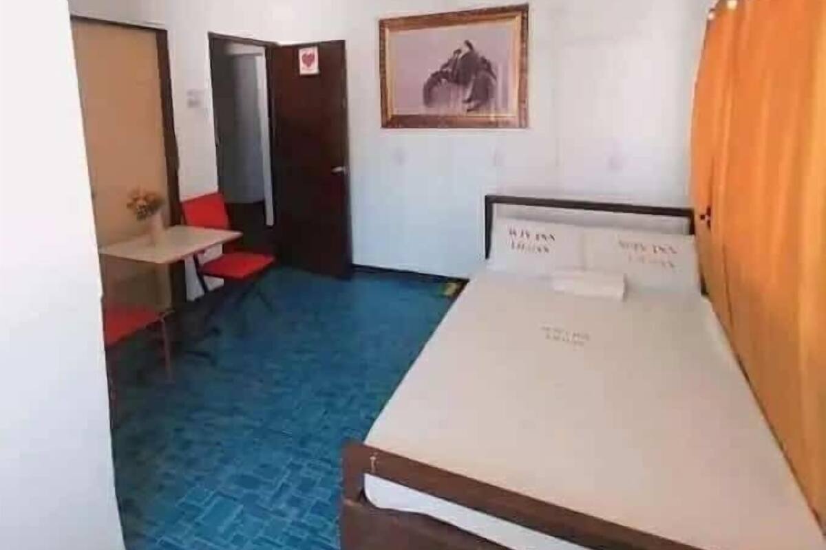 A room with a bed, a desk, and a chair. There is a door leading to another room.