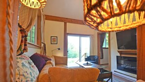 A cozy living room with a sofa, a TV, and a large window. - Welcome to the Meadowverse, your peaceful retreat (Galiano Island)
