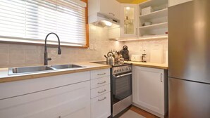 A modern kitchen with white cabinets, a stainless steel sink, a stove, and a refrigerator. - Welcome to the Meadowverse, your peaceful retreat (Galiano Island)