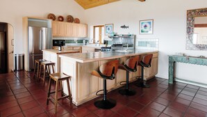 A spacious kitchen with a large island, wooden bar stools, and a tiled backsplash. - Salto Retreat, Valley Views, HotTub, Patio, Hiking (Arroyo Seco)