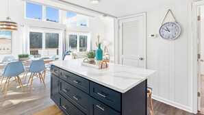 Une cuisine moderne dotée d’un grand îlot central, de meubles de rangement aux couleurs sombres et offrant une vue sur l’extérieur.