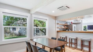Una cocina moderna con una mesa de madera y taburetes de bar, ventanas amplias con vistas a la vegetación y un horno empotrado.