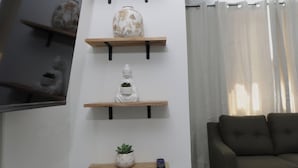 A modern living room with a vertical wooden shelf unit displaying various decorative items, a grey sofa, and a staircase to the left. - Oceanview Apartment with Rooftop (Terranova)