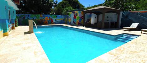 A swimming pool with a tiled deck, a lounge chair, and a colorful mural on the wall.