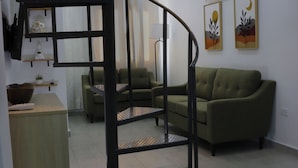 A modern living room with a spiral staircase, a green sofa, and a small table. - Oceanview Apartment with Rooftop (Terranova)