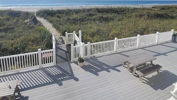 Eine Holzterrasse mit weißen Geländern, die auf einen Strand blickt.
