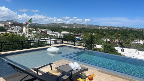 Une piscine sur le toit, avec des chaises longues, un panier de fruits et une boisson servie sur un plateau.