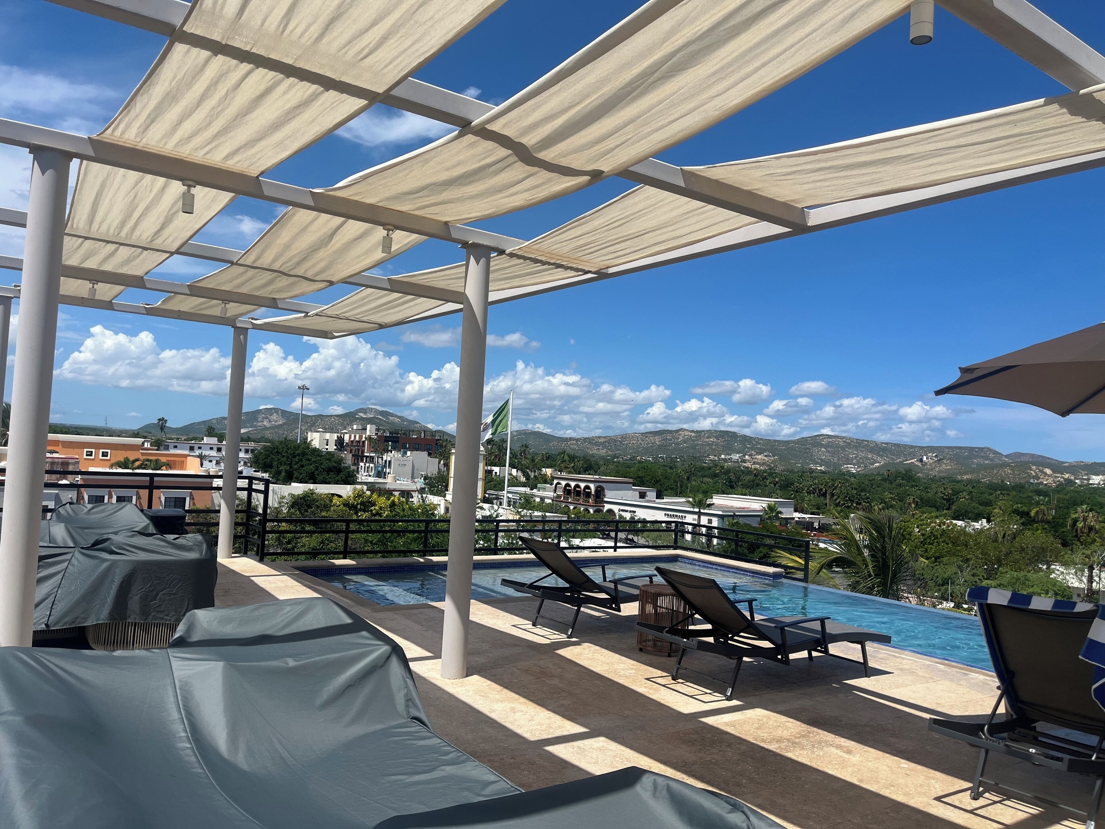 A poolside area with lounge chairs, a covered seating area, and a view of the surrounding landscape.