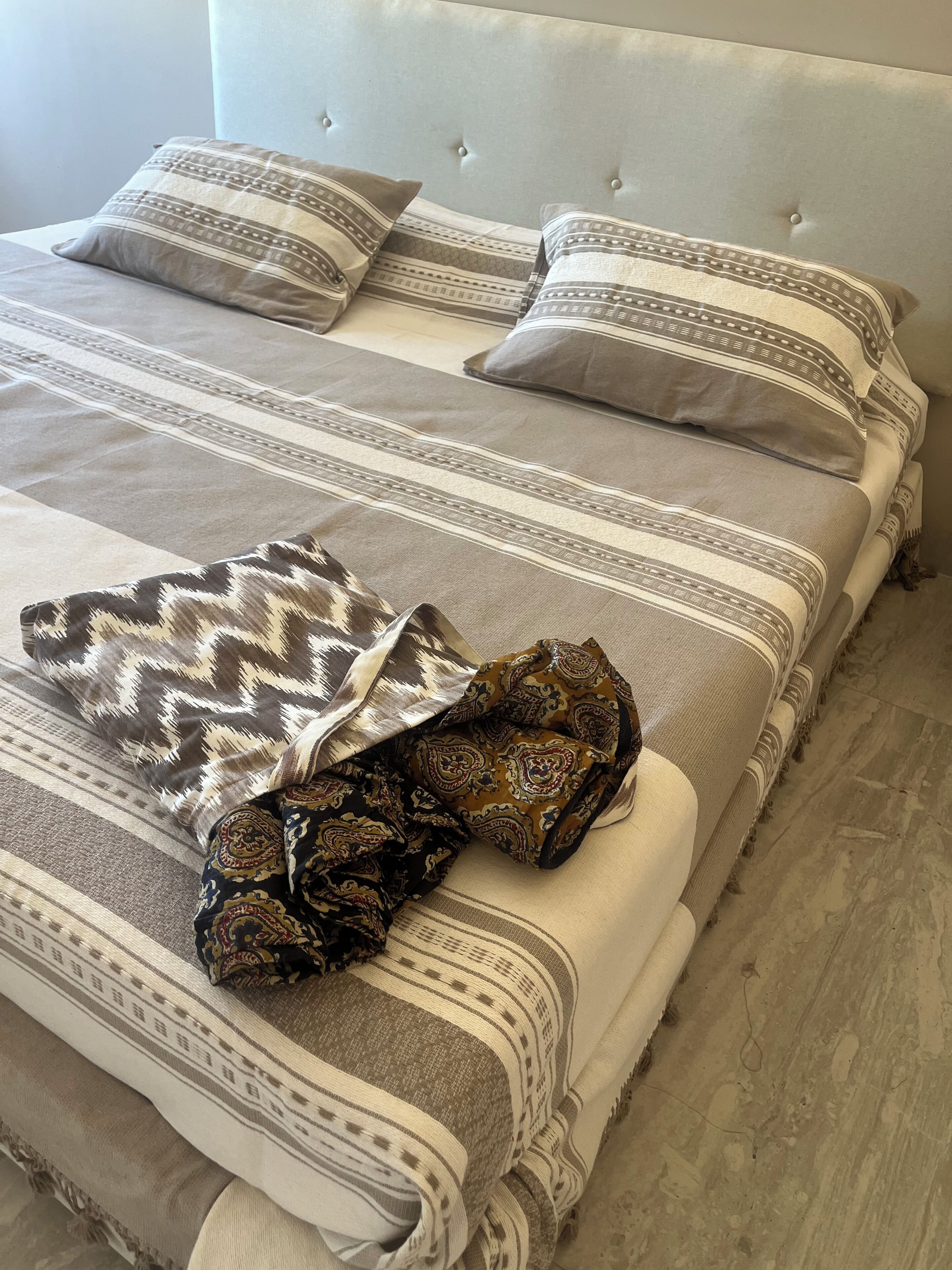 Uma cama com roupa de cama listrada, almofadas decorativas e um cobertor estampado, além de uma cabeceira.