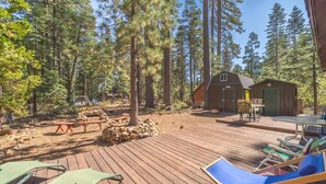 Una terraza de madera con mobiliario exterior, un cobertizo pequeño y un paisaje boscoso de fondo.