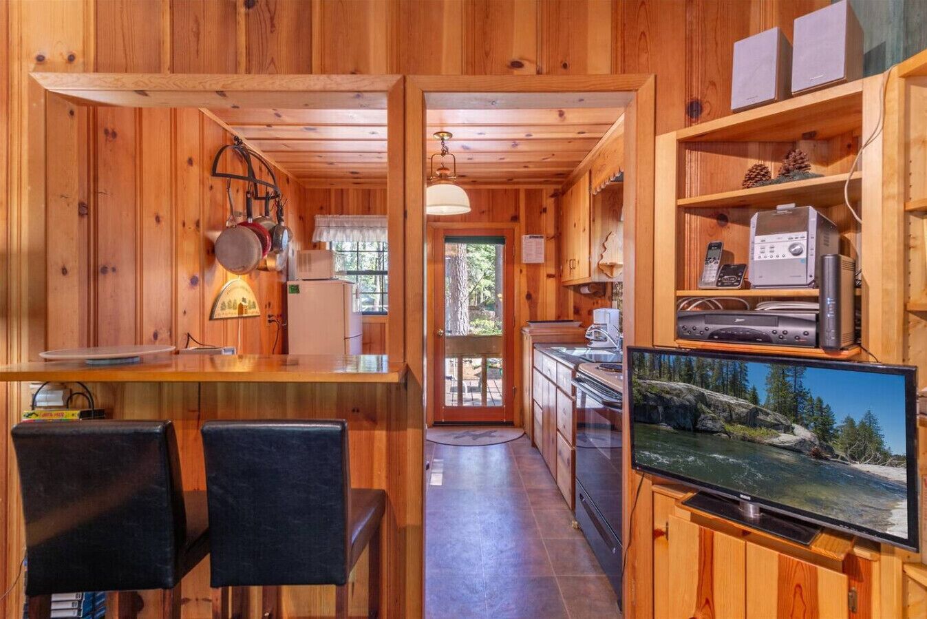 Ein Interieur einer Holzhütte mit Küche, Essbereich und Fernseher, der eine Naturaufnahme zeigt.