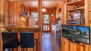 Interior de una cabaña de madera con cocina, comedor y televisor mostrando una escena natural.
