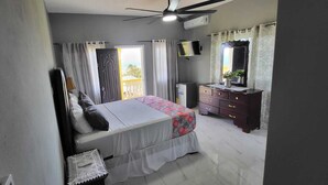 A bedroom with a bed, a dresser, a television, and a ceiling fan. - Kingsbird by the sea Inn  (Discovery Bay)