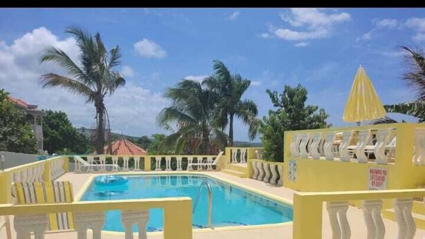 A swimming pool with yellow railings and palm trees in the background. - Kingsbird by the sea Inn  (Discovery Bay)