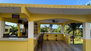 A yellow bar area with a counter, stools, and a view of the outdoors. - Kingsbird by the sea Inn  (Discovery Bay)