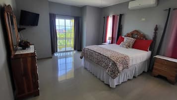 A bedroom with a bed, a dresser, a TV, and a window with curtains.